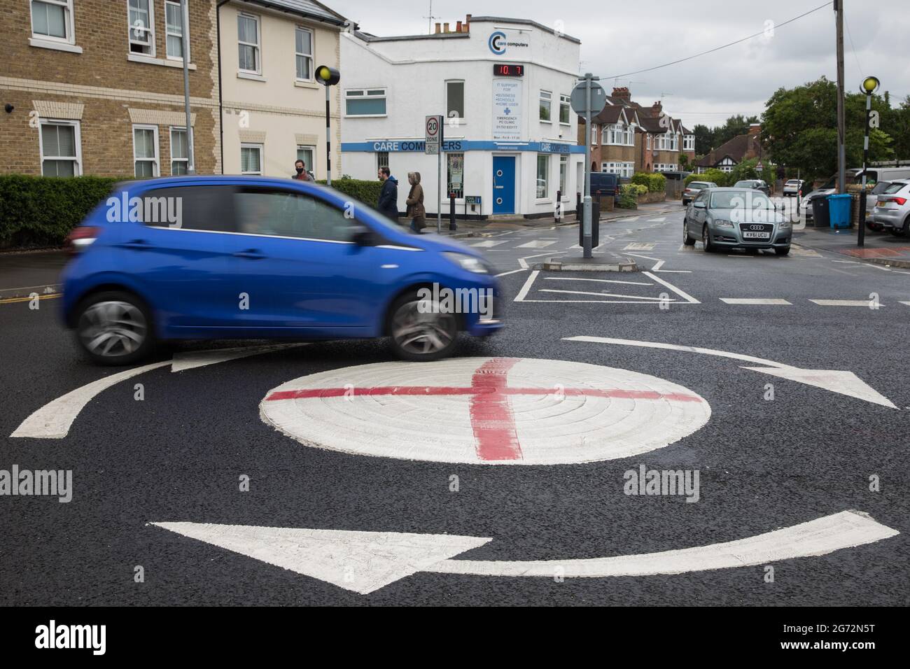 Windsor, UK. 10th July, 2021. A blue vehicle passes a mini-roundabout painted with the St George's flag. The Royal Borough of Windsor and Maidenhead repainted several roundabouts for safety reasons previously daubed with England flags before England's Euro 2020 quarter-final match against Ukraine but it appears that local residents have restored them in advance of the Euro 2020 final between England and Italy. Credit: Mark Kerrison/Alamy Live News Stock Photo