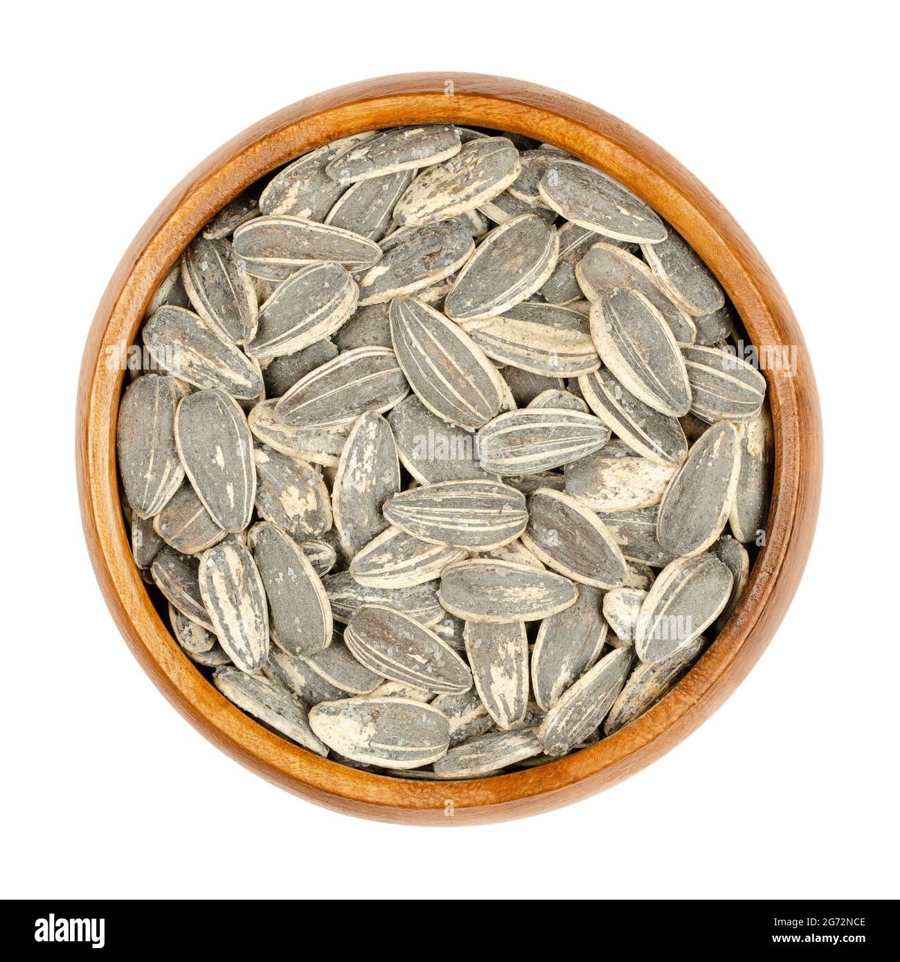 Large sunflower seeds in shells roasted and salted, in a wooden bowl. Whole striped common sunflower seeds, fruits of Helianthus Annuus. Stock Photo
