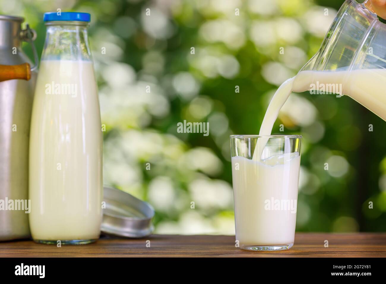 milk pouring from jug into glass outdoors Stock Photo