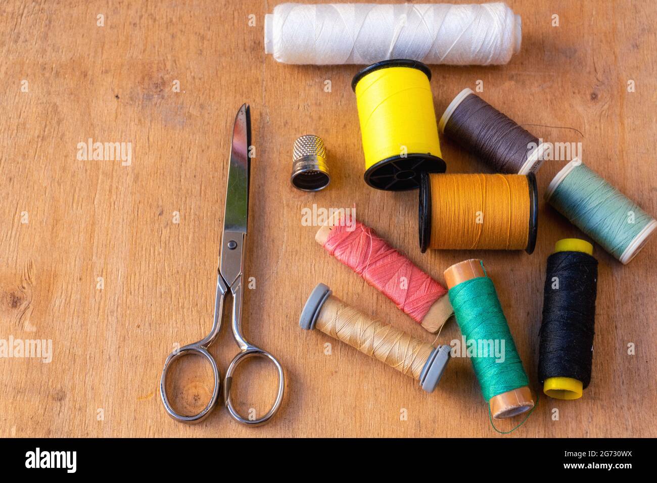 Top view of colored thread spools, thimbles, and scissors on a wooden background Stock Photo