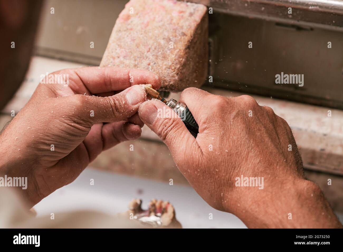 Dental technician shaping a part of a dental prosthesis with a electric tool Stock Photo