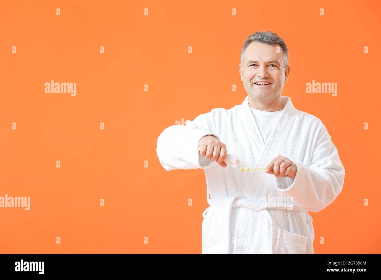 Mature man brushing teeth on color background Stock Photo