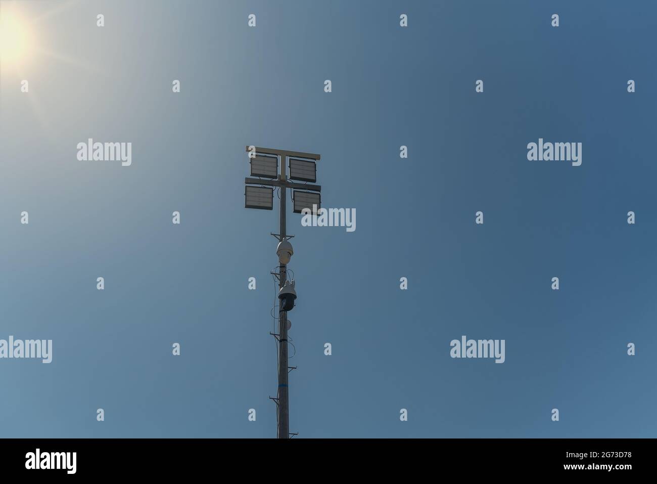 A street pole with surveillance cameras, in a criminal zone, and night lighting lamps. Against the blue sky and sun. Stock Photo