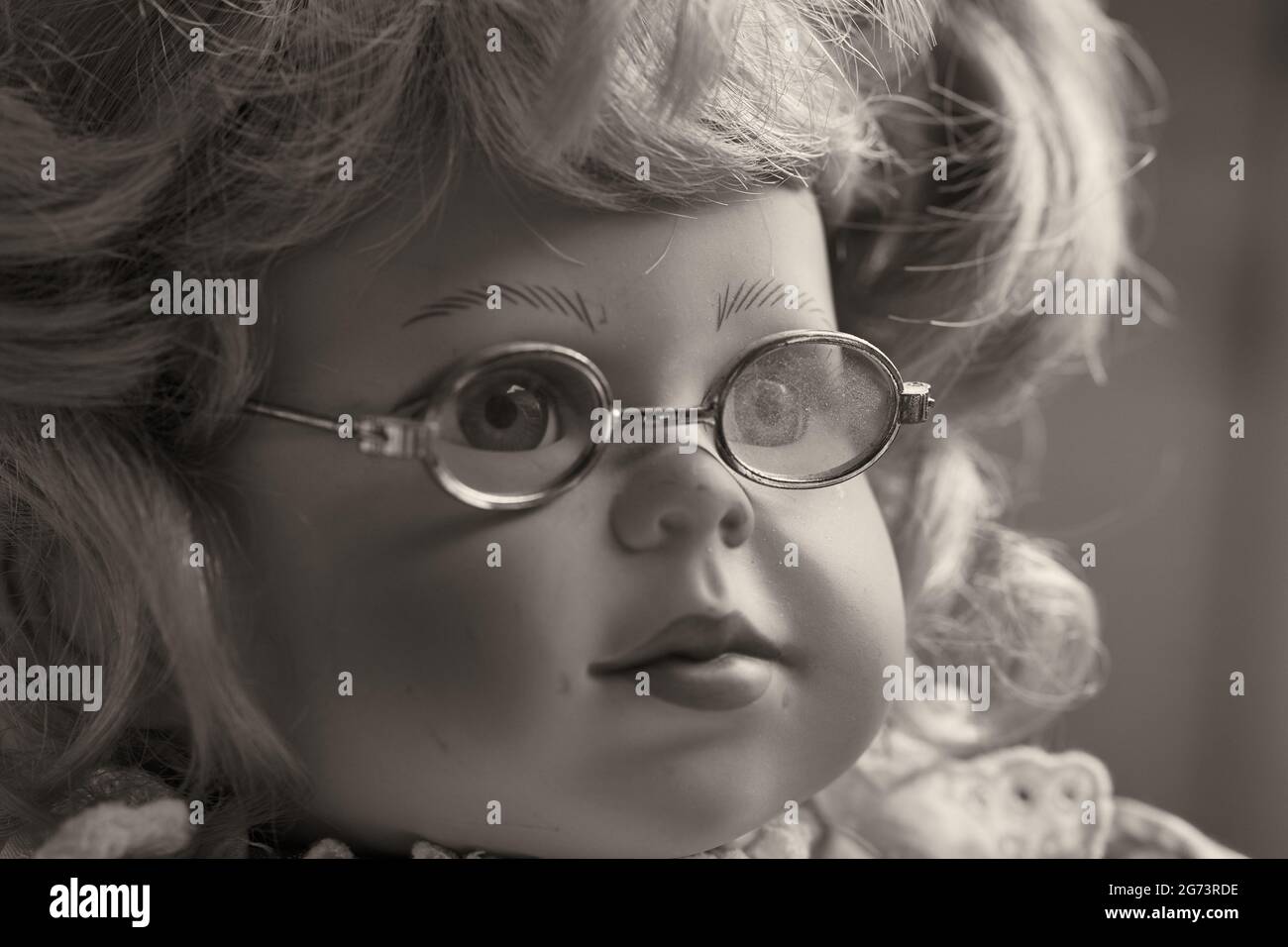 Portrait of a vintage baby doll, a toy girl with blond hair and glasses. Stock Photo