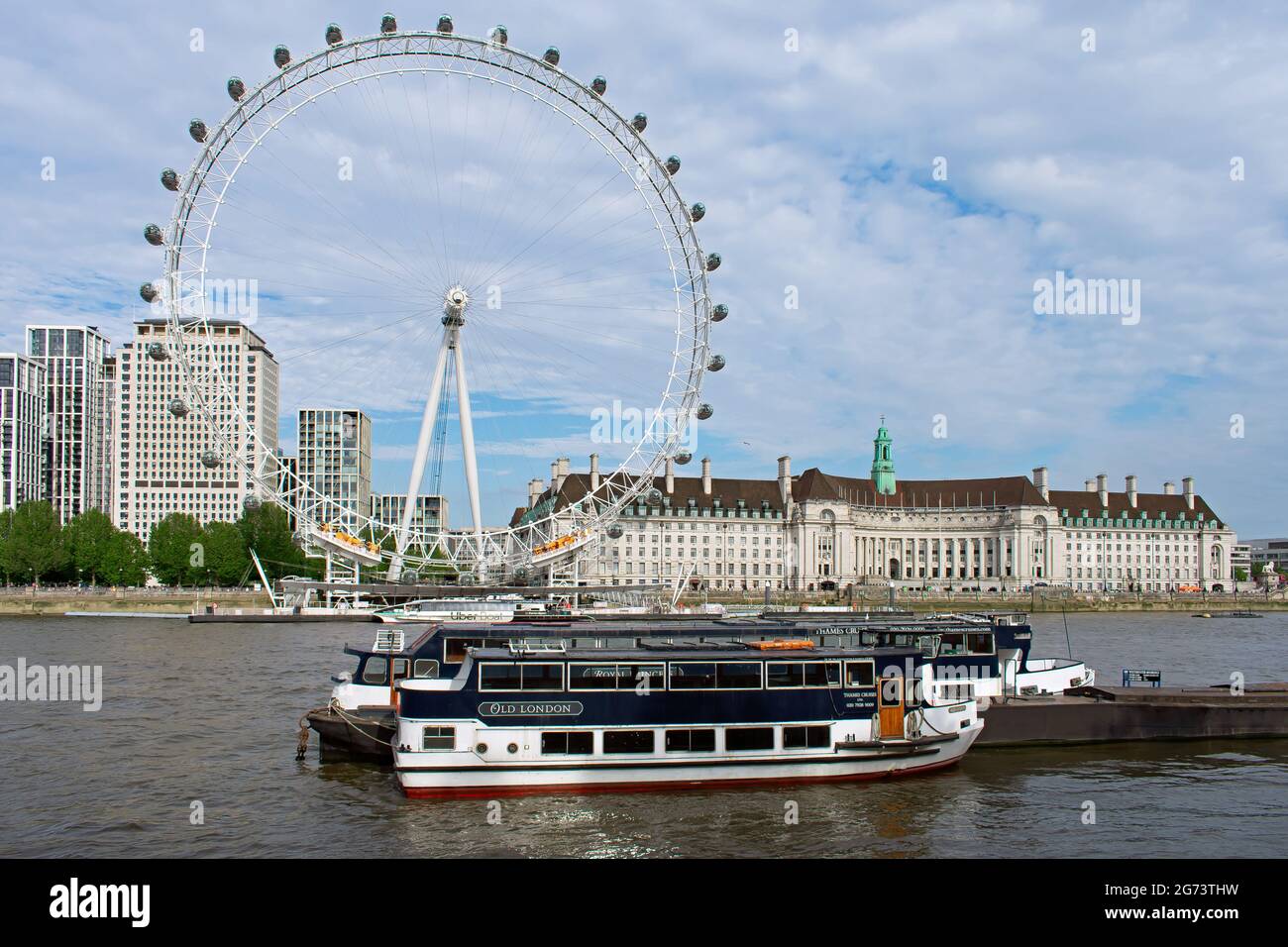 Two boats moored directly across the River Thames from the London Eye. County Hall on the southern side of the river next to the tourist attraction. Stock Photo