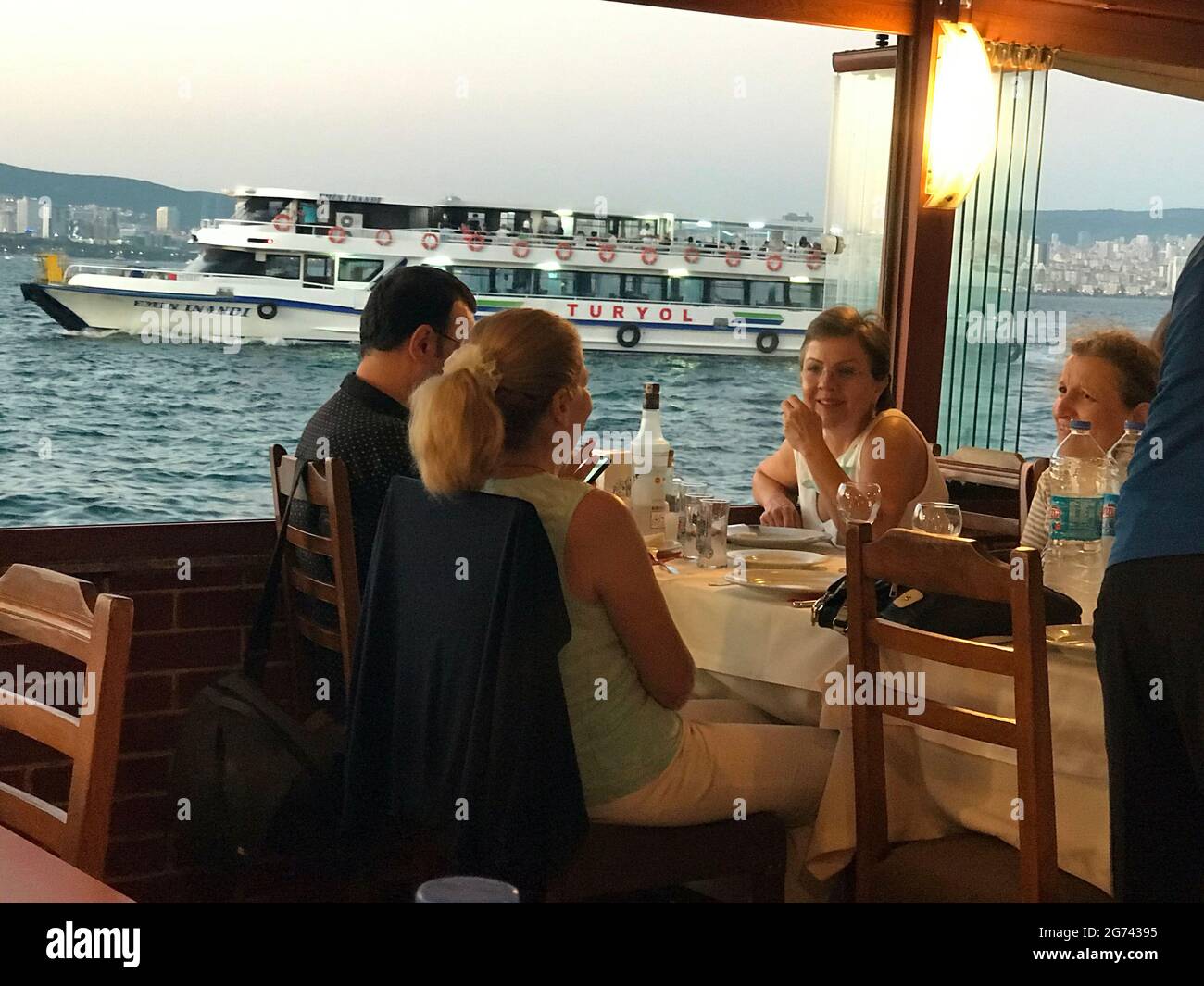 People having dinner in a restaurant alongside the Bosphorous Sea as a ferry boat passes the Princess Islands in Istanbul, Turkey Stock Photo
