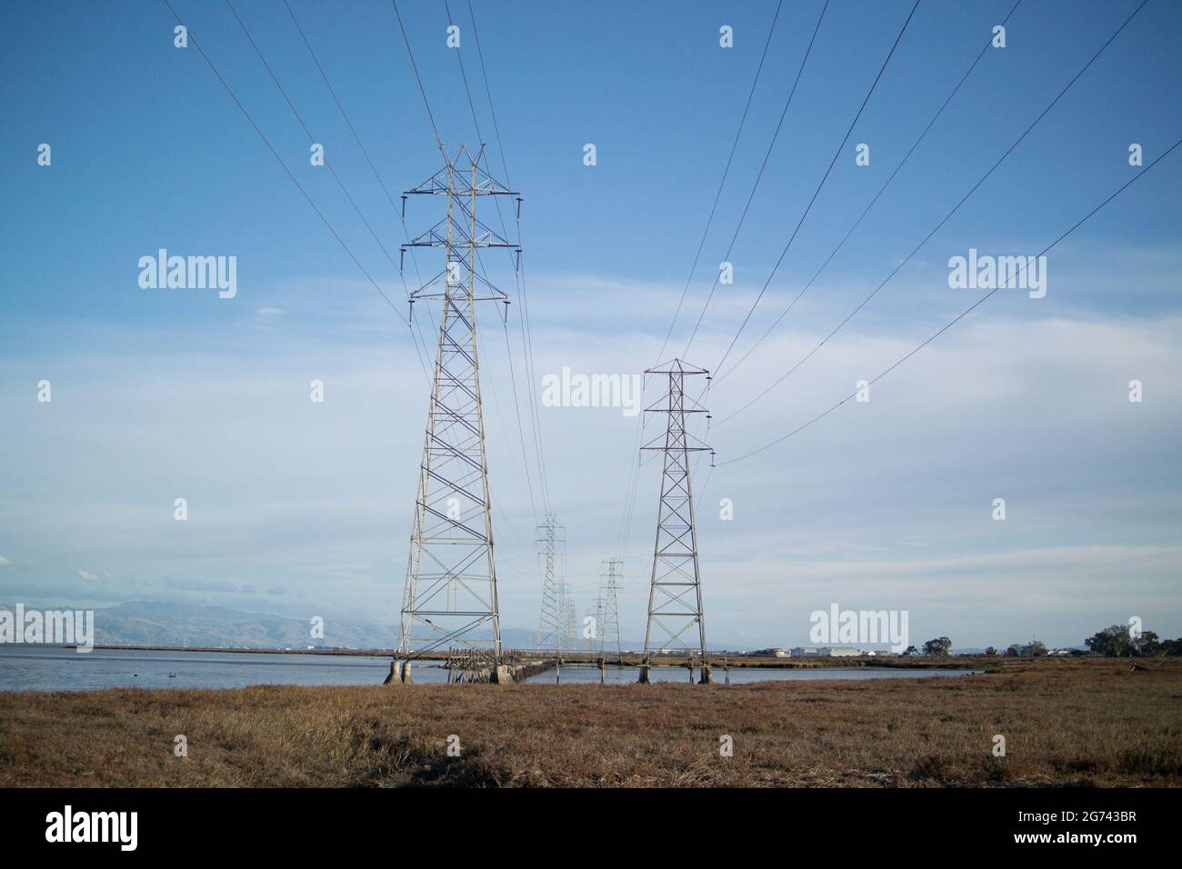 Transmission towers in two lines with overhead power cables going over marshland on San Francisco Bay Stock Photo