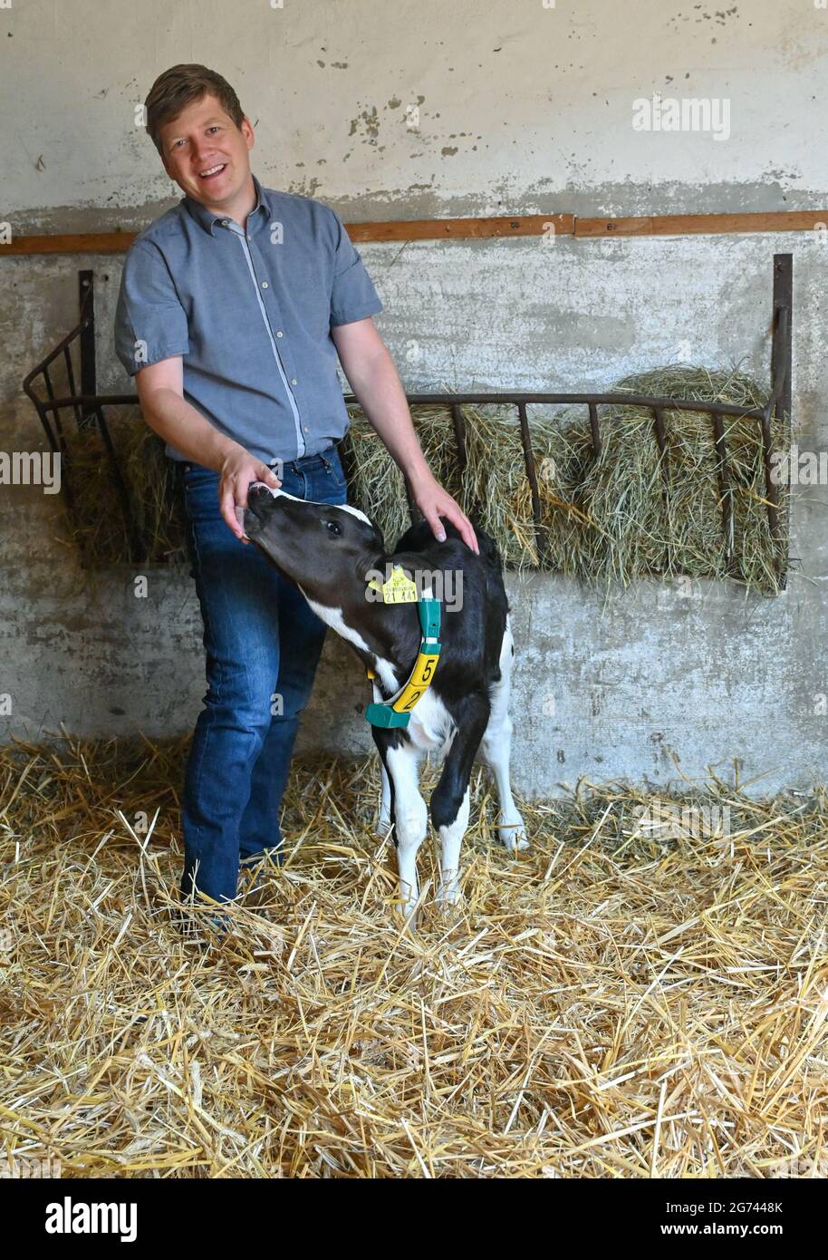Klein Mutz, Germany. 06th July, 2021. Andreas Paries, farmer, stands in a  barn with a young calf. Since the beginning of the year, the farm he runs  with his mother and brother