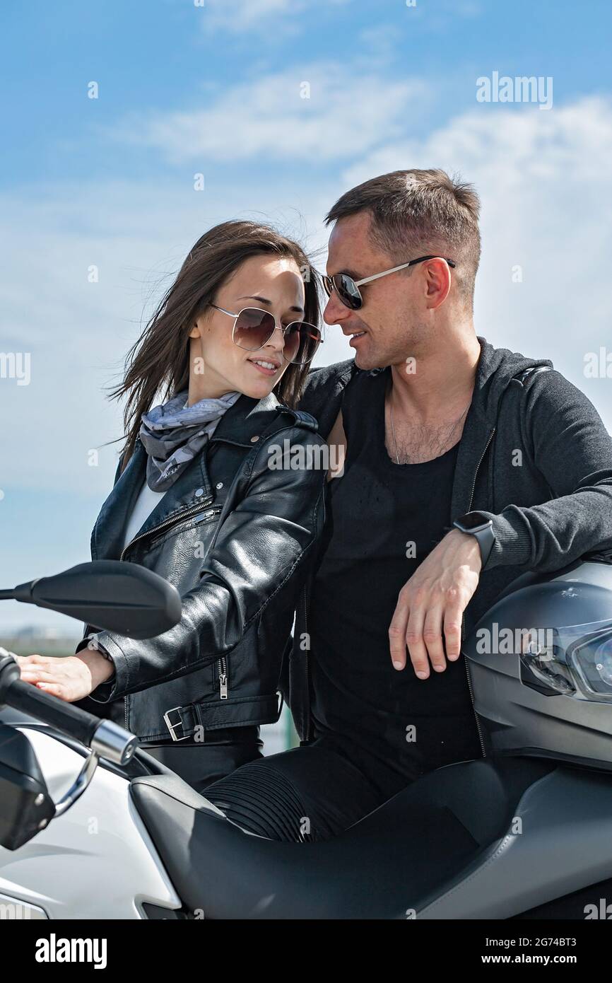 Two attractive people in sunglasses. Smiling handsome biker with beautiful pretty cheerful woman. Models are posing near the motorcycle. Vertical shot Stock Photo