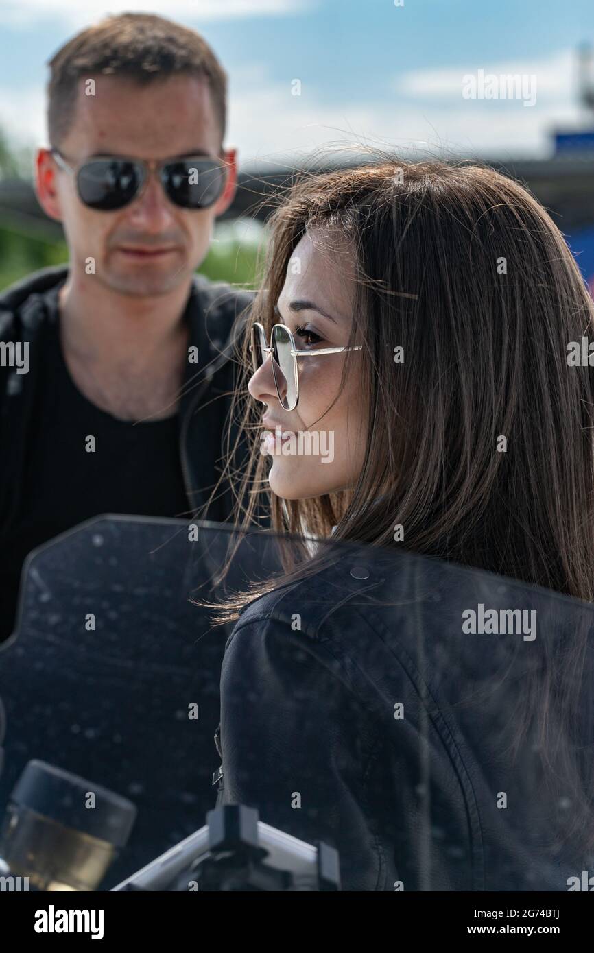 Attractive beautiful young caucasian couple. Smiling couple in love in sunglasses. Guy and girl are standing in leather jackets near the motorbike. Ve Stock Photo