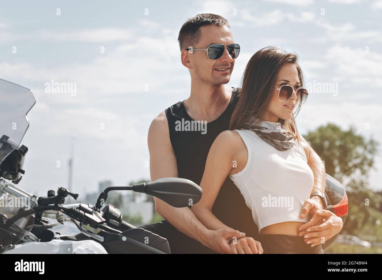 Cheerful smiling couple in love in sunglasses. Handsome man and pretty woman are hugging. Young attractive people are posing on the motorbike. Horizon Stock Photo