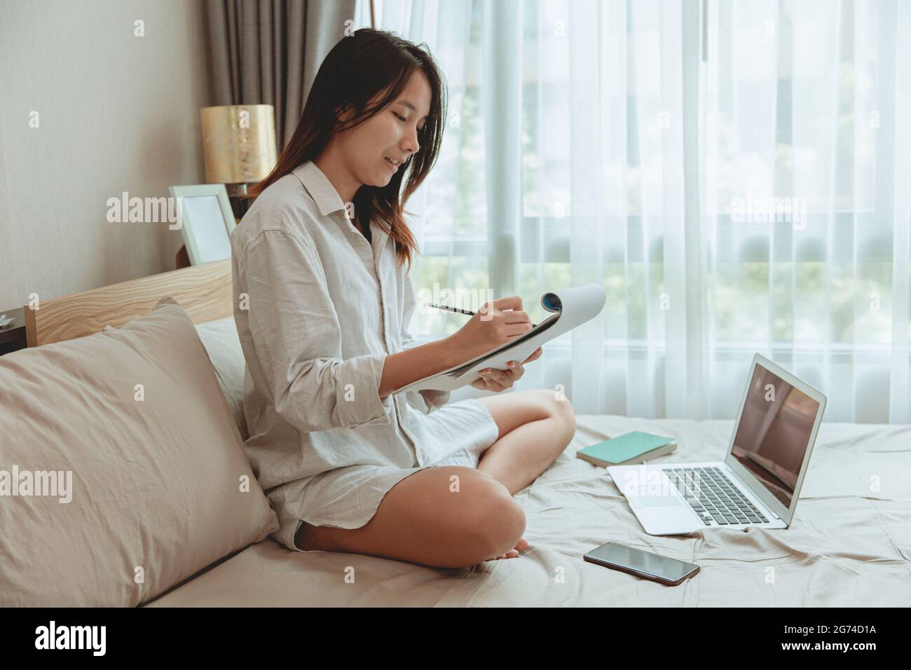 Girl teen working study at home during covid lockdown self quarantine, women comfortable holiday writing homework on the bed. Stock Photo