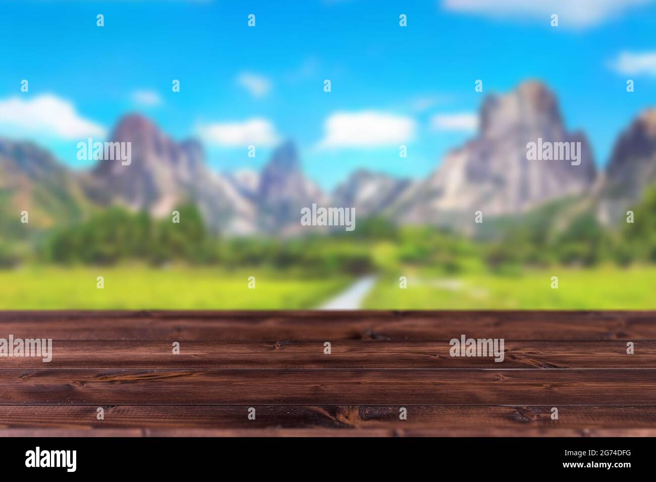 Blur beautiful green nature mountain view blue sky with wooden table foreground space for products advertising montage background. Stock Photo