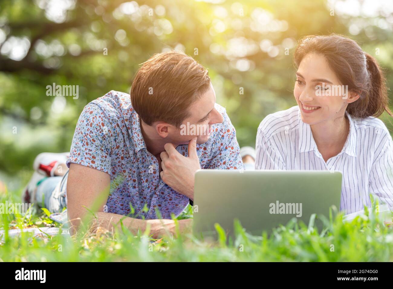 Couple male and women lover using laptop online wireless technology outdoor in the park in holiday vacation together. Stock Photo