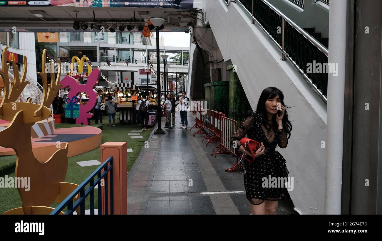 Asian Lady Walking Talking on Mobile Phone Wearing Black Dress Carry Red Purse on Sukhumvit Road Bangkok Thailand Christmas Time Stock Photo