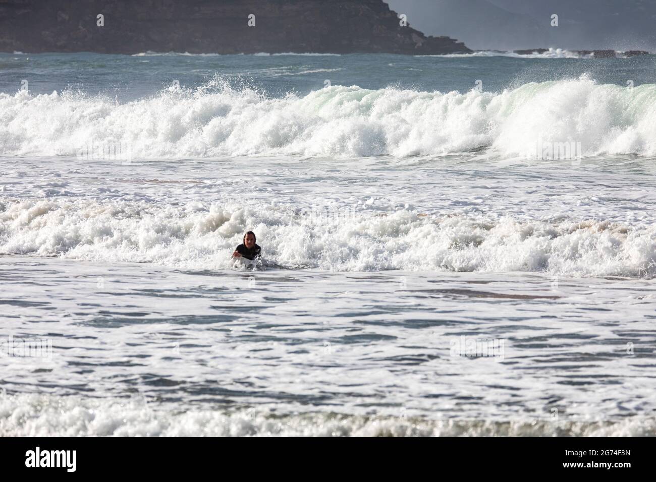 Australian surfer heads to shore with big waves behind at Palm Beach in