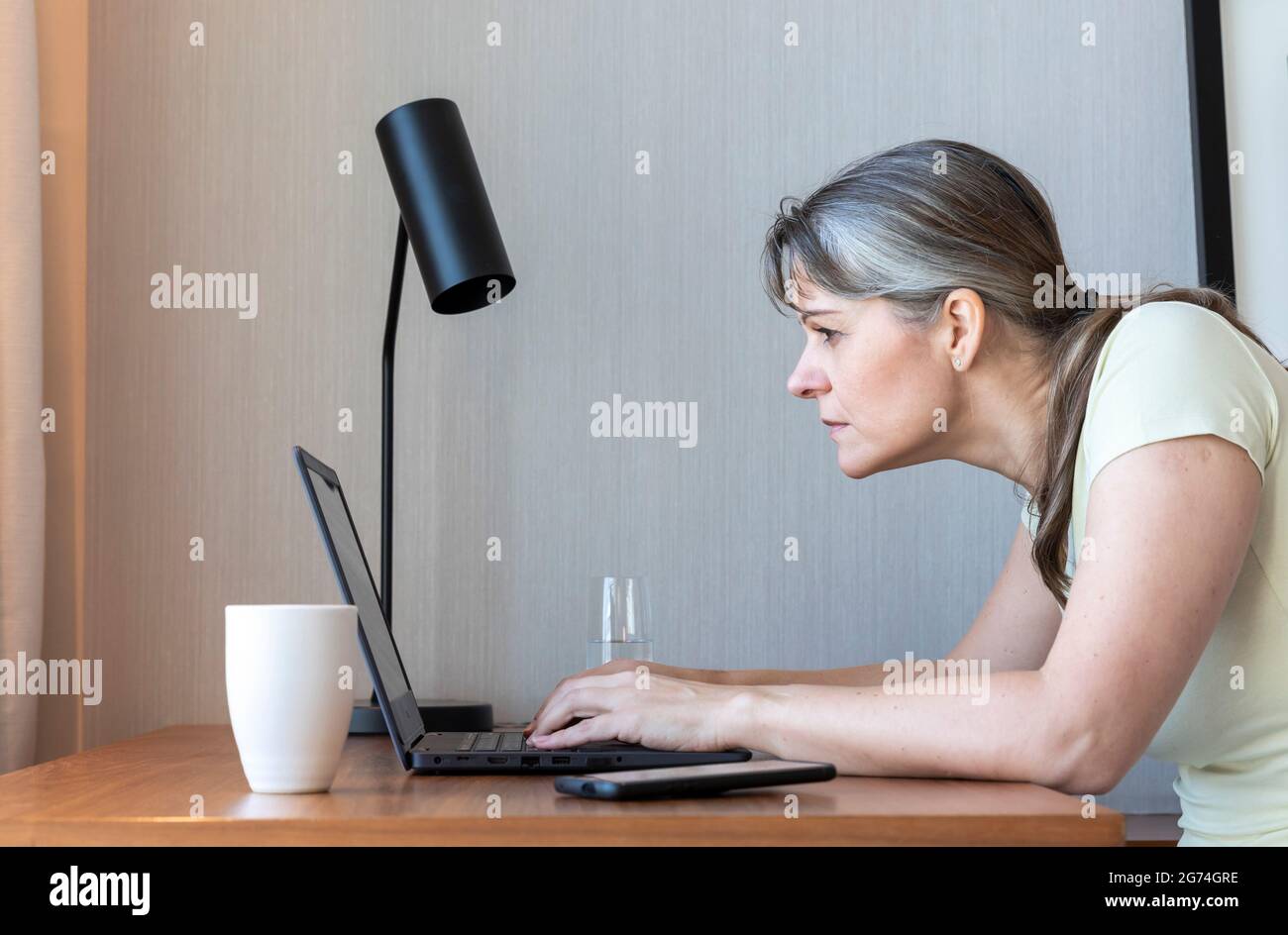 Woman with a poor eyesight working in her laptop, struggling to see ...