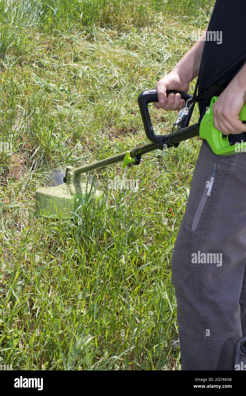 A man with an electric lawn mower mows the grass. For a gardening equipment store, vertical photo. Stock Photo