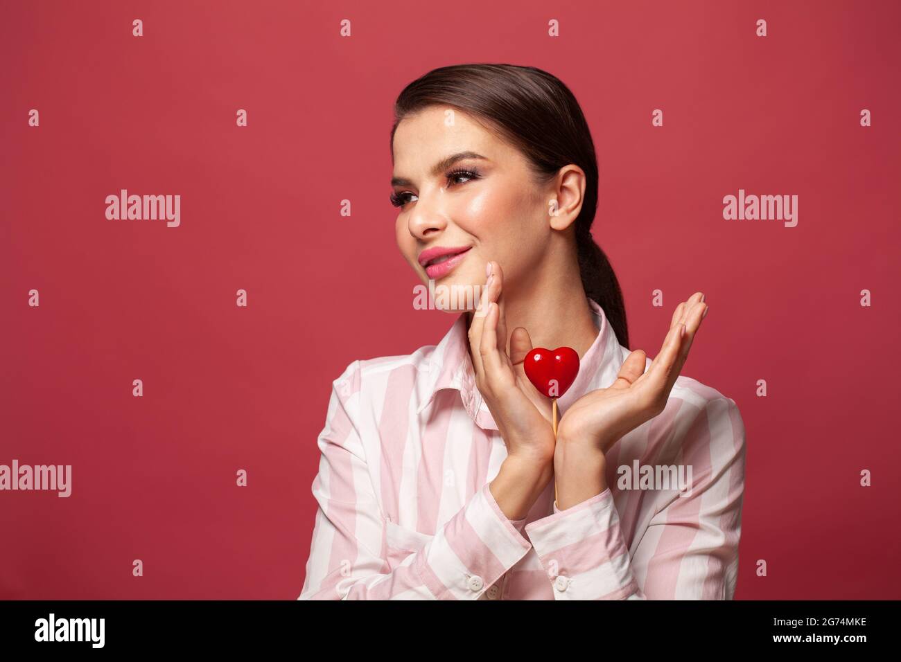 Young brunette woman holding red heart in her hands on pink background ...