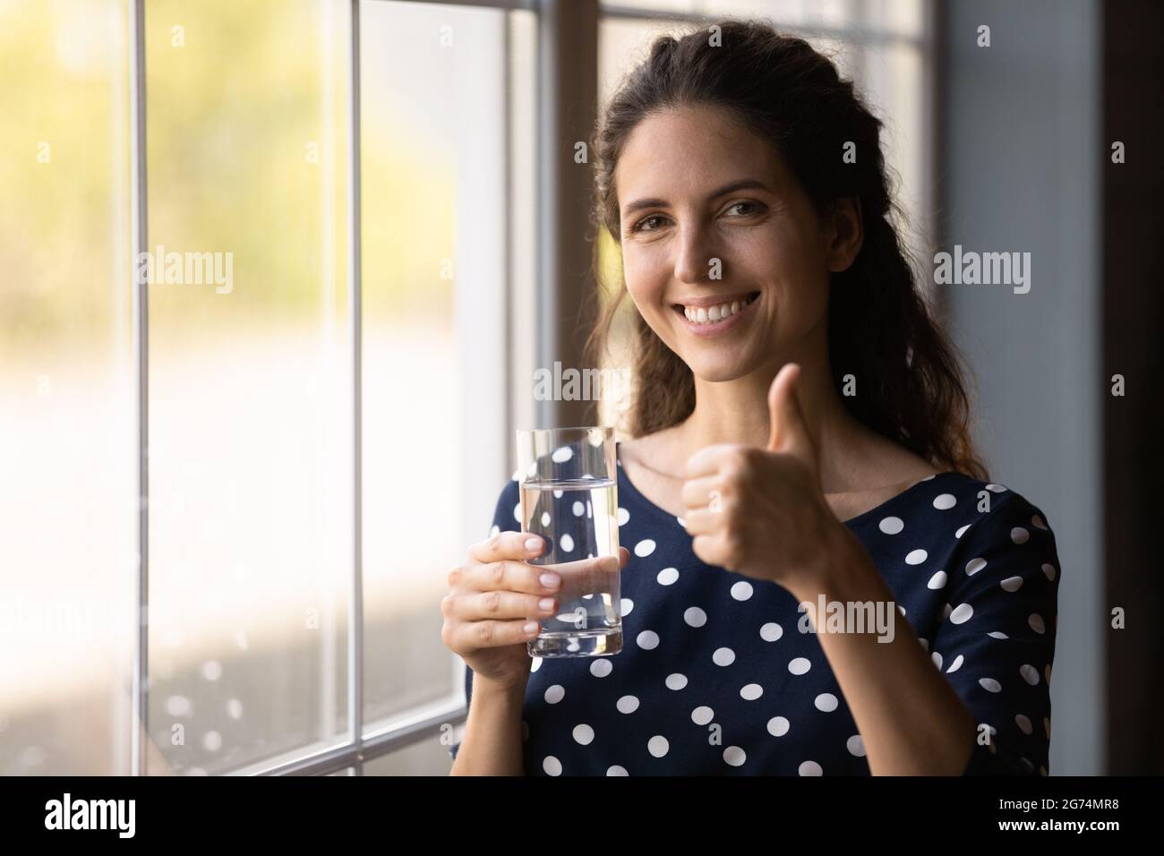 Happy Hispanic woman drinking fresh water, holding transparent glass Stock Photo