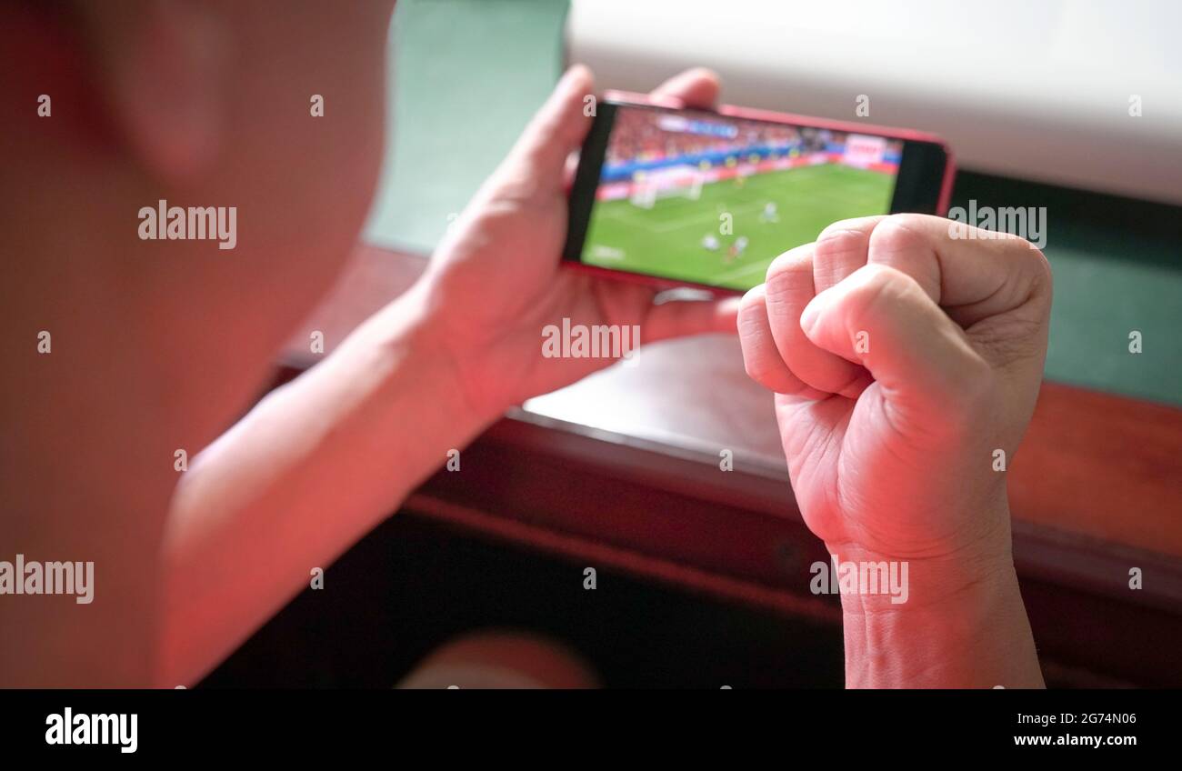 Sports fan with fist up in celebration while watching sports streaming on mobile phone. Close up view. Stock Photo