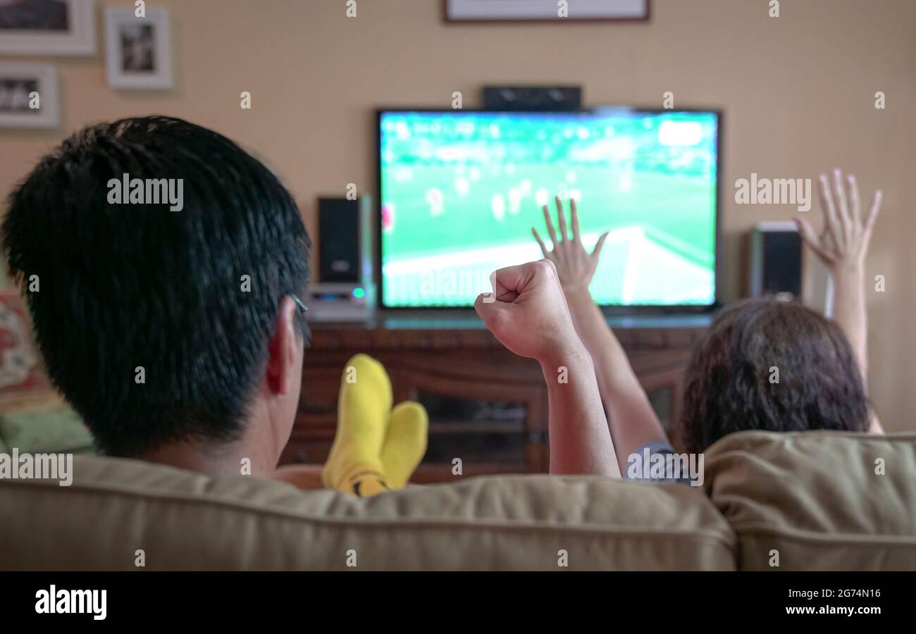 People watching sports streaming on tv, cheering with fist and hands raised. Stay at home. Stock Photo