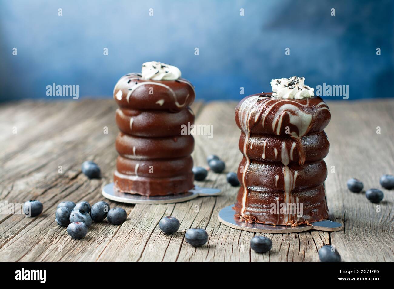 Egg cakes with chocolate glaze, topped with whipped cream, decorated with chocolate sprinkles. Blueberries are scattered on the weathered wood planks. Stock Photo