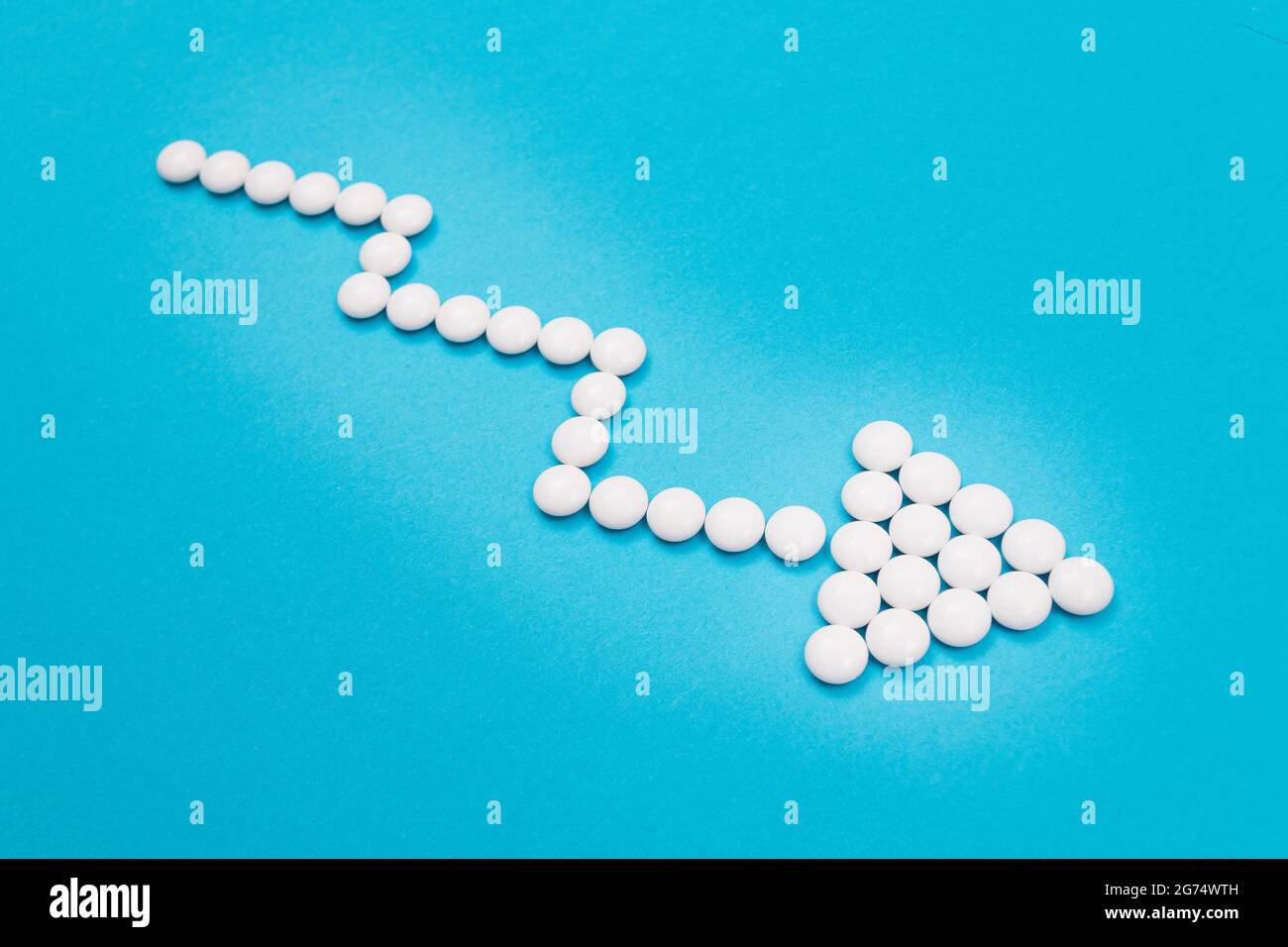 Global Pharmaceutical Industry and Medicinal Products - Downward Arrow Made from White Pills on Blue Background Stock Photo
