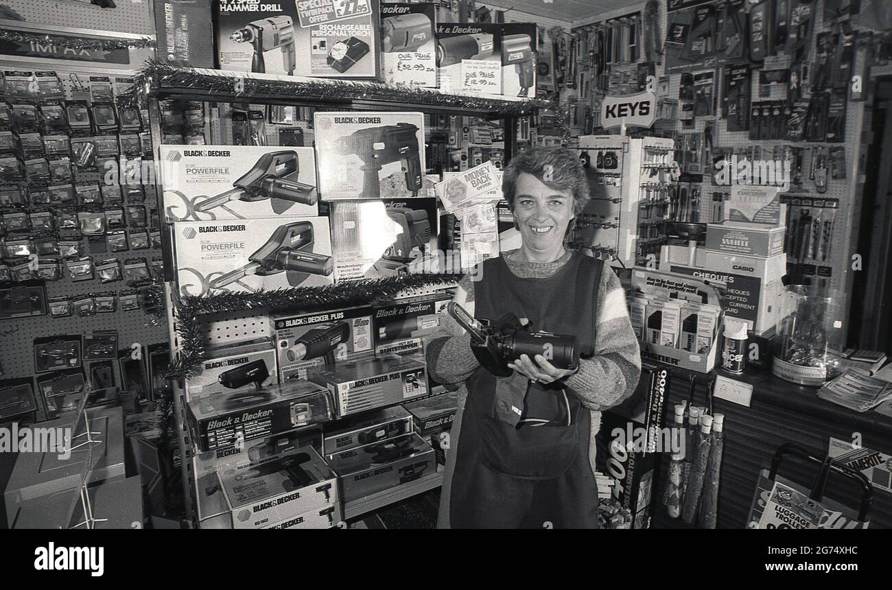 https://c8.alamy.com/comp/2G74XHC/1980s-historical-a-lady-shopkeeper-of-a-hardware-store-standing-in-a-pinafore-over-a-sweater-she-is-showing-the-latest-handtool-drill-a-blackdecker-powerfile-belt-sander-england-uk-2G74XHC.jpg