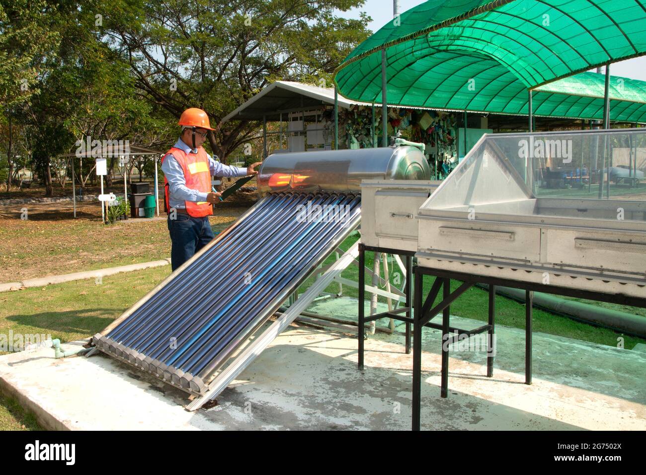 The Asian worker in uniform and helmet checks concentrating Solar Power with Flat Plat collector and Evacuum Tube Collector. Stock Photo