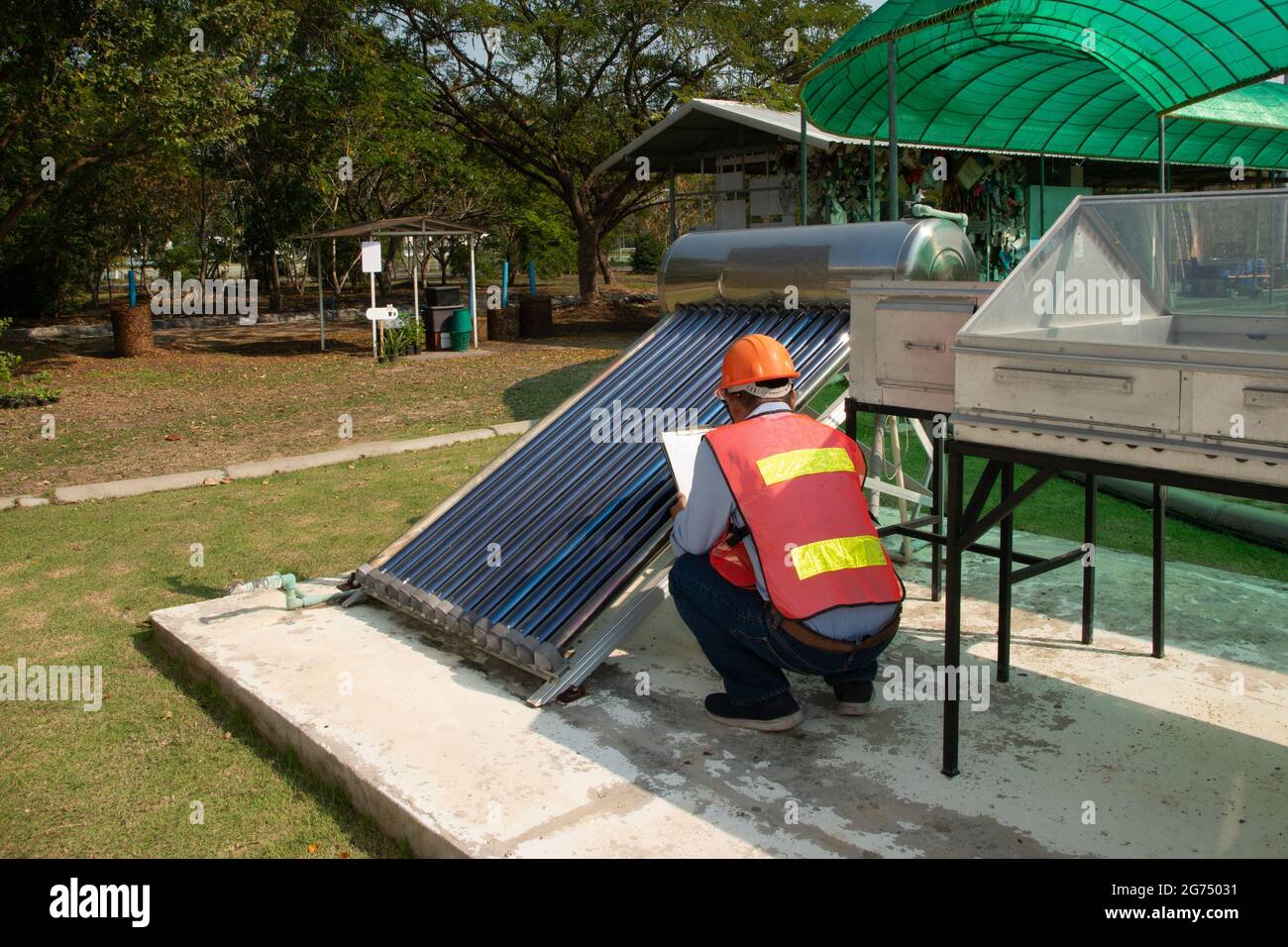 The Asian worker in uniform and helmet checks concentrating Solar Power with Flat Plat collector and Evacuum Tube Collector. Stock Photo