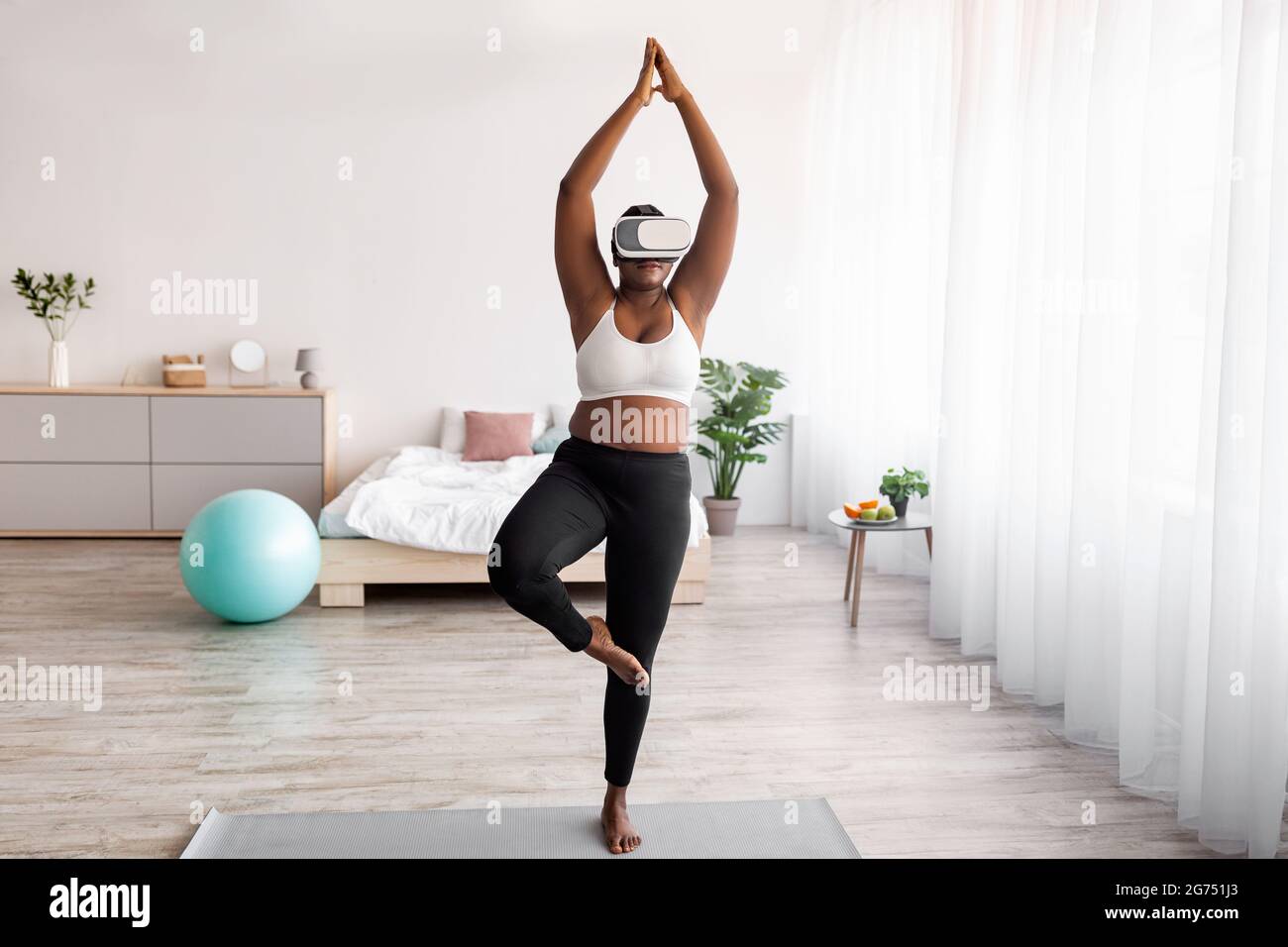 Overweight black lady wearing VR headset, practicing yoga in augmented