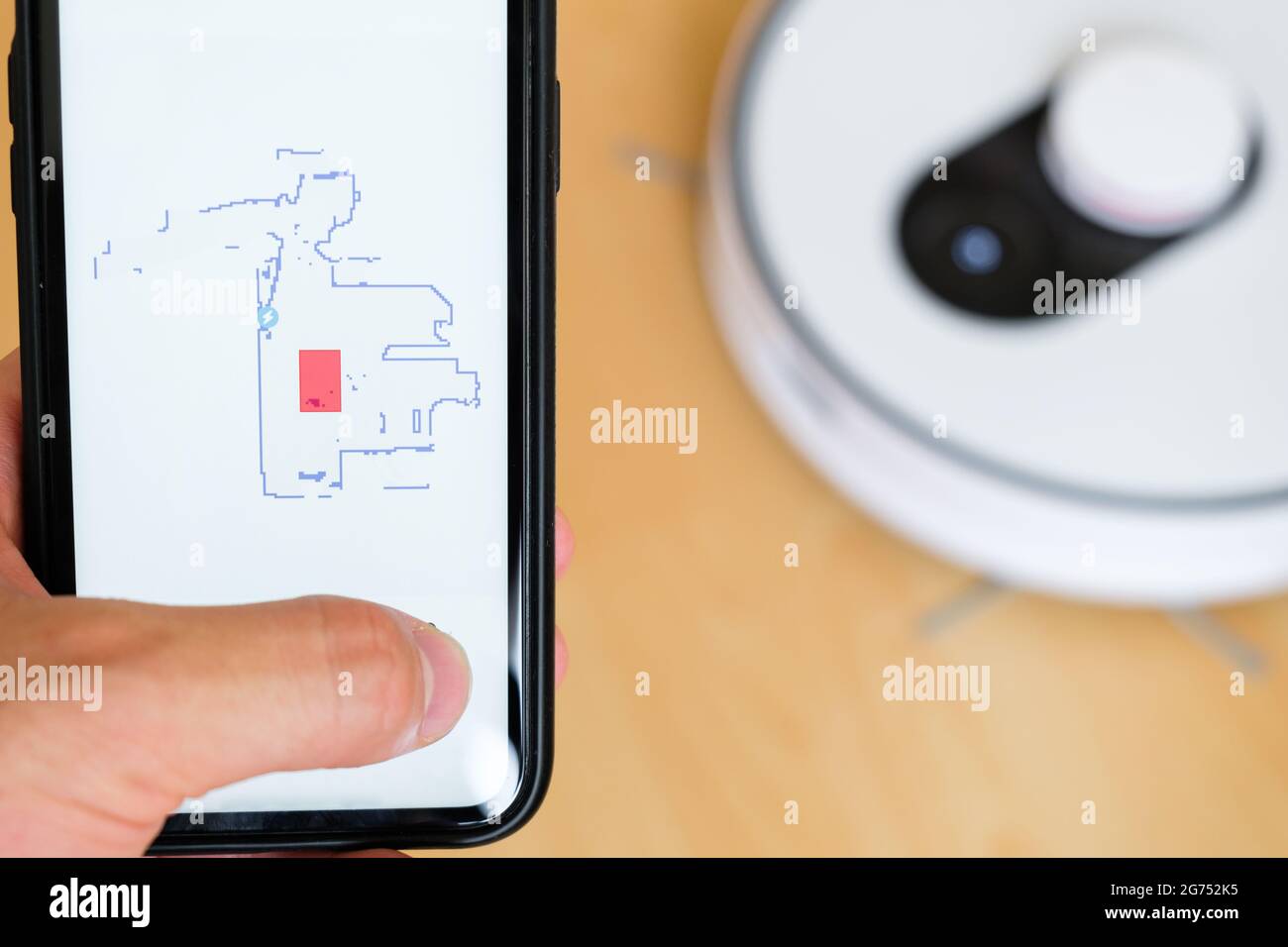 Close up a mobile phone application for managing of robot vacuum cleaner in mans hand. Smart technology for housekeeping  Stock Photo