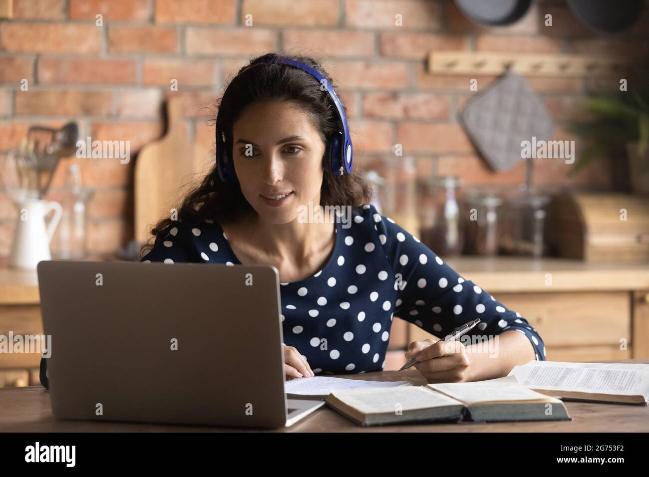 Happy focused female adult student with headphones and laptop Stock Photo