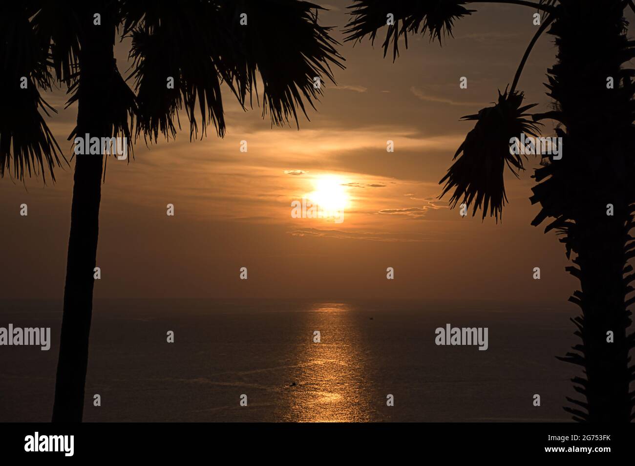 Beautiful stunning scenic panoramic view of the golden sky and reflections on the Andaman sea with palm trees during the sunset at Promthep Cape landm Stock Photo