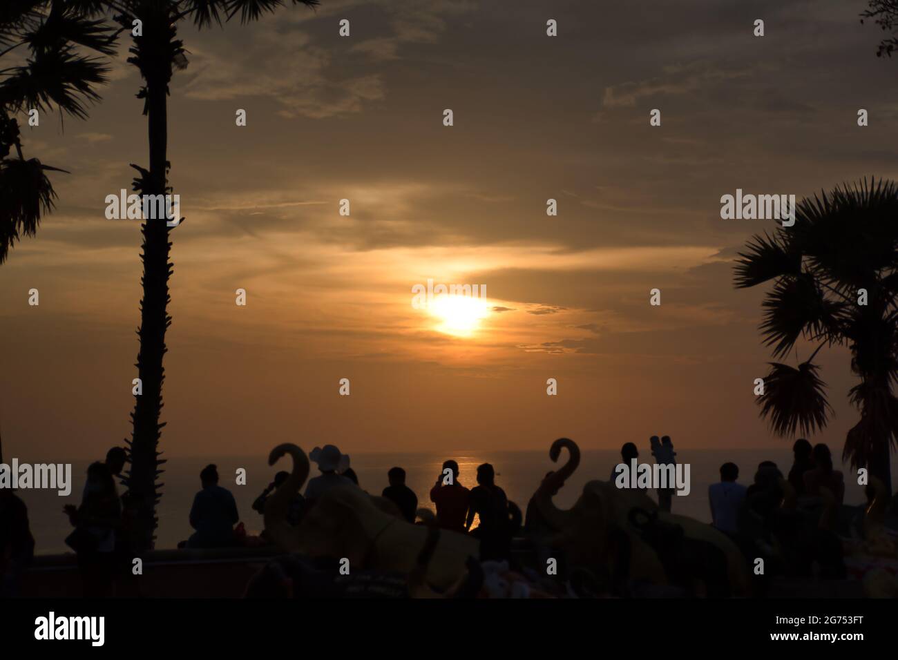 Beautiful stunning scenic panoramic view of the golden sky reflections on the Andaman sea with silhouettes of palm trees people during the sunset at P Stock Photo