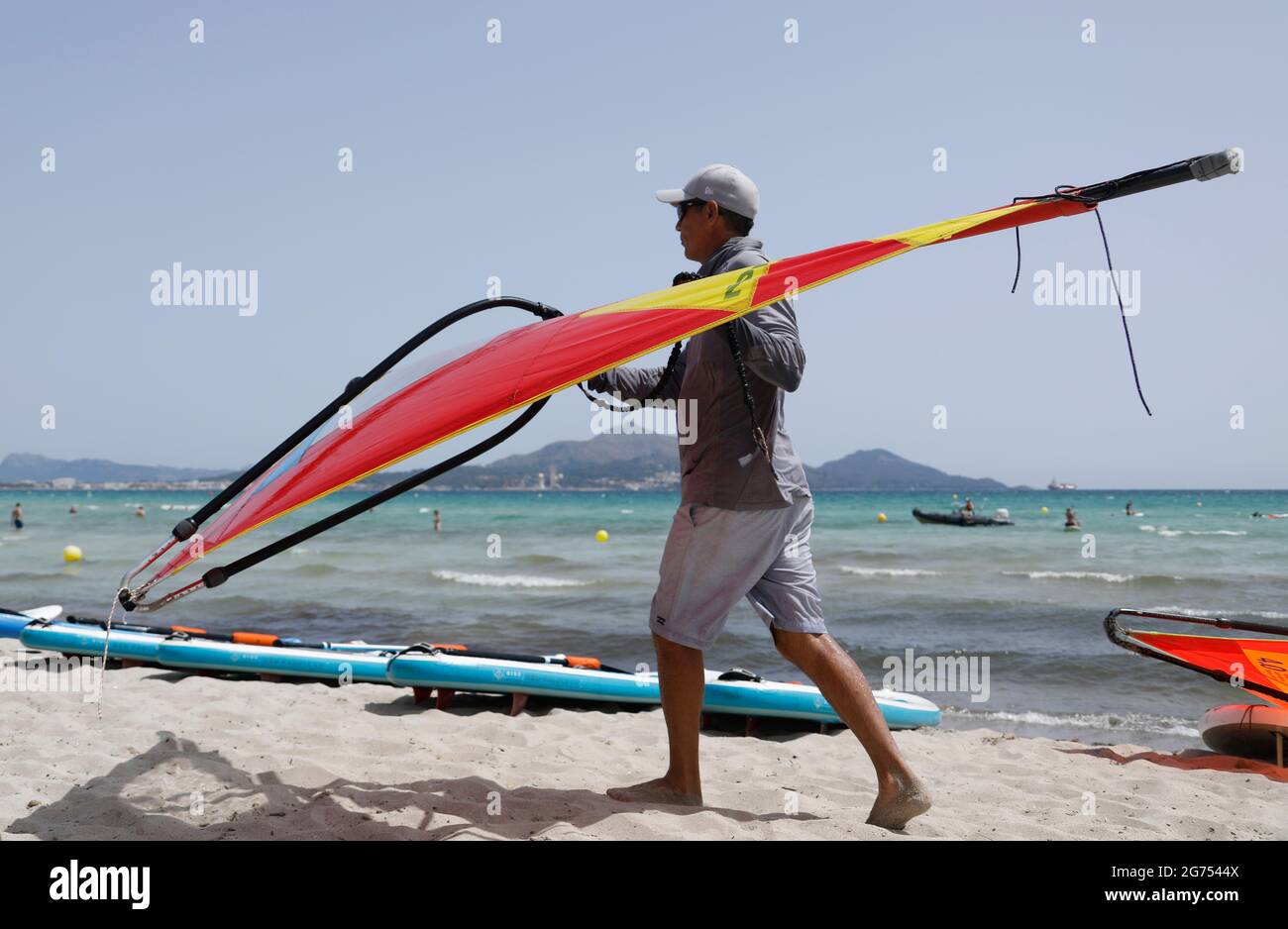 Maorca, Spain. 11th July, 2021. An instructor of a water sports school prepares surfboards for windsurfing on the beach of Playa de Muro in the north of Mallorca. The federal government has declared all of Spain with Mallorca and the Canary Islands in view of rapidly increasing Corona numbers to the risk area. The practical effects for Mallorca holidaymakers are limited for the time being. Credit: Clara Margais/dpa/Alamy Live News Stock Photo