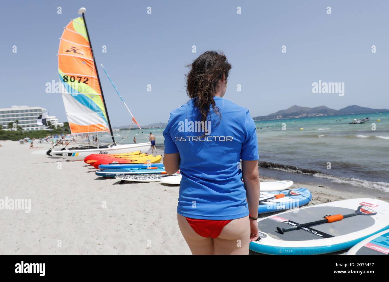 Maorca, Spain. 11th July, 2021. Anna, the teacher of a water sports school, prepares surfboards for windsurfing on the beach of Playa de Muro in the north of Mallorca. The federal government has declared the whole of Spain, including Mallorca and the Canary Islands, a risk area in view of rapidly rising Corona numbers. The practical effects for Mallorca holidaymakers are limited for the time being. Credit: Clara Margais/dpa/Alamy Live News Stock Photo
