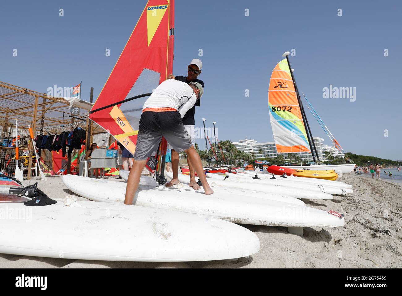 Maorca, Spain. 11th July, 2021. Teachers of a water sports school set up surfboards for windsurfing on the beach of Playa de Muro in the north of Mallorca. The federal government has declared all of Spain with Mallorca and the Canary Islands in view of rapidly increasing Corona numbers to the risk area. The practical effects for Mallorca holidaymakers are limited for the time being. Credit: Clara Margais/dpa/Alamy Live News Stock Photo