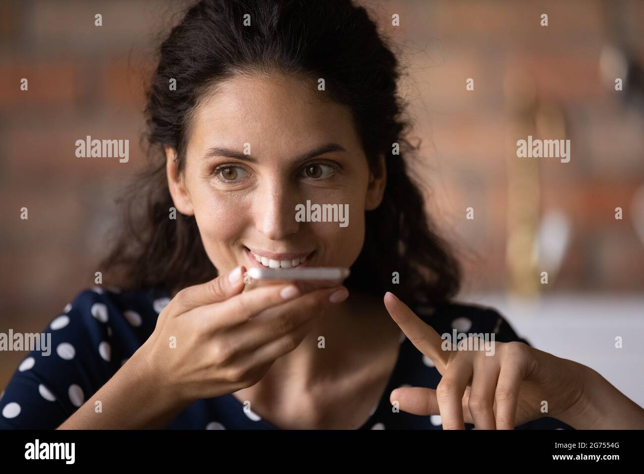 Happy Latin woman with cellphone recording audio message Stock Photo