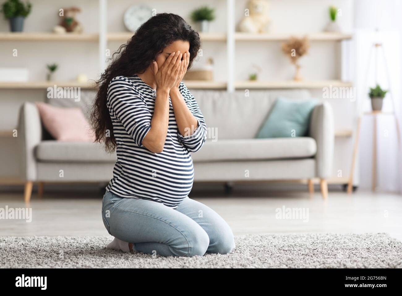 Young pregnant woman feeling down and crying at home Stock Photo
