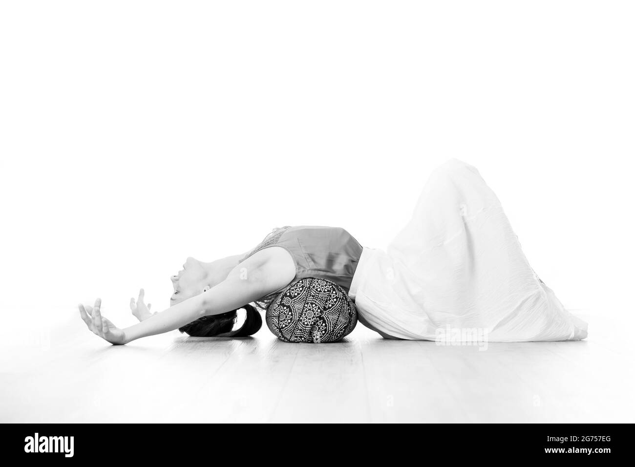 Restorative yoga with a bolster. Young sporty attractive woman in bright white yoga studio, stretching and relaxing during restorative yoga with Stock Photo
