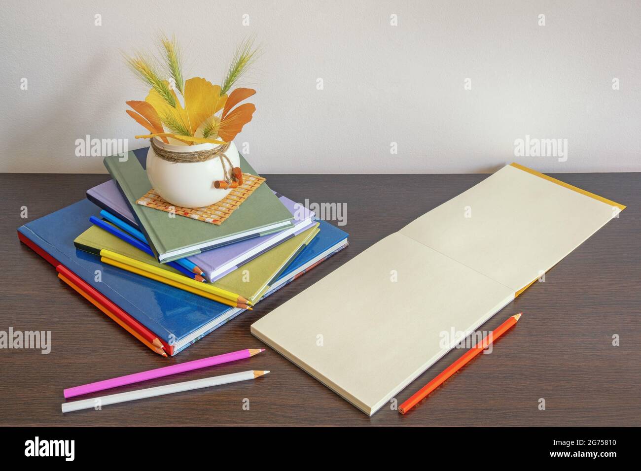 School concept. Stack of books, colorful colored pencils and open sketchbook on dark background. Autumn leaves. Free space for text or picture Stock Photo