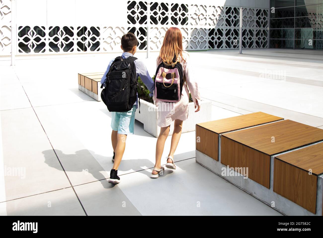 Children, teenagers, schoolchildren boy and girl on background of concrete wall go to school building. View from back. Back to school Stock Photo