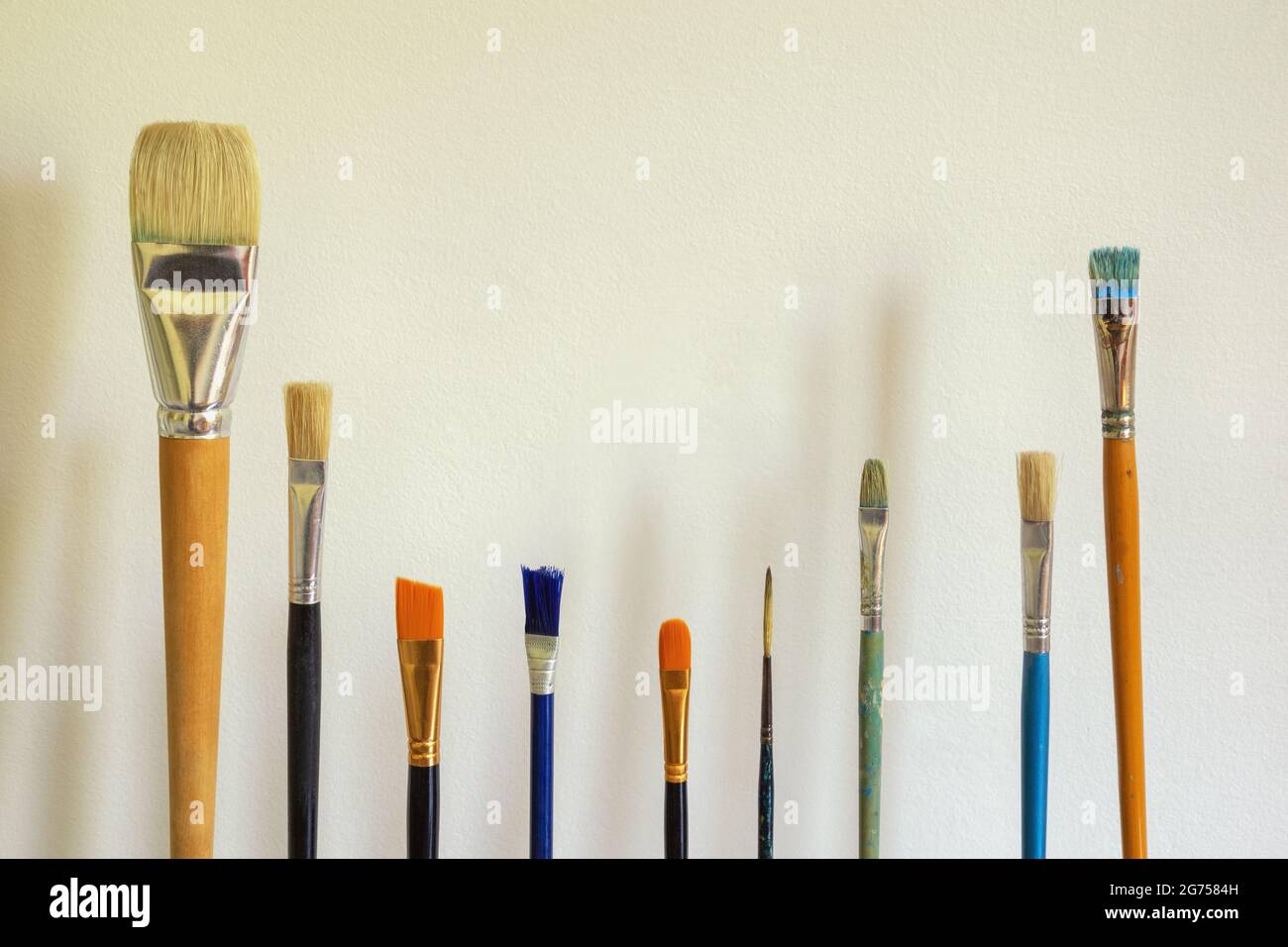 Different paint brushes against white rustic wall. Free space for text