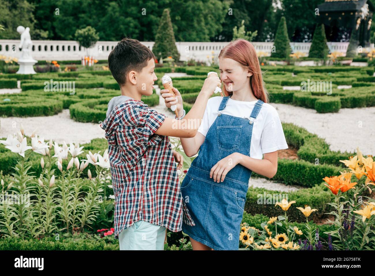children teenagers boy and girl are having fun on summer day against background of greenery, eating ice cream Stock Photo