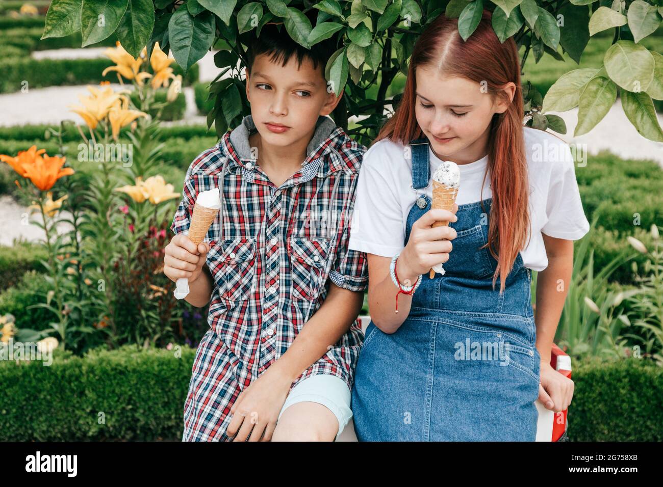 children teenagers boy, girl are having fun on summer day against background of greenery, eating ice cream together Stock Photo