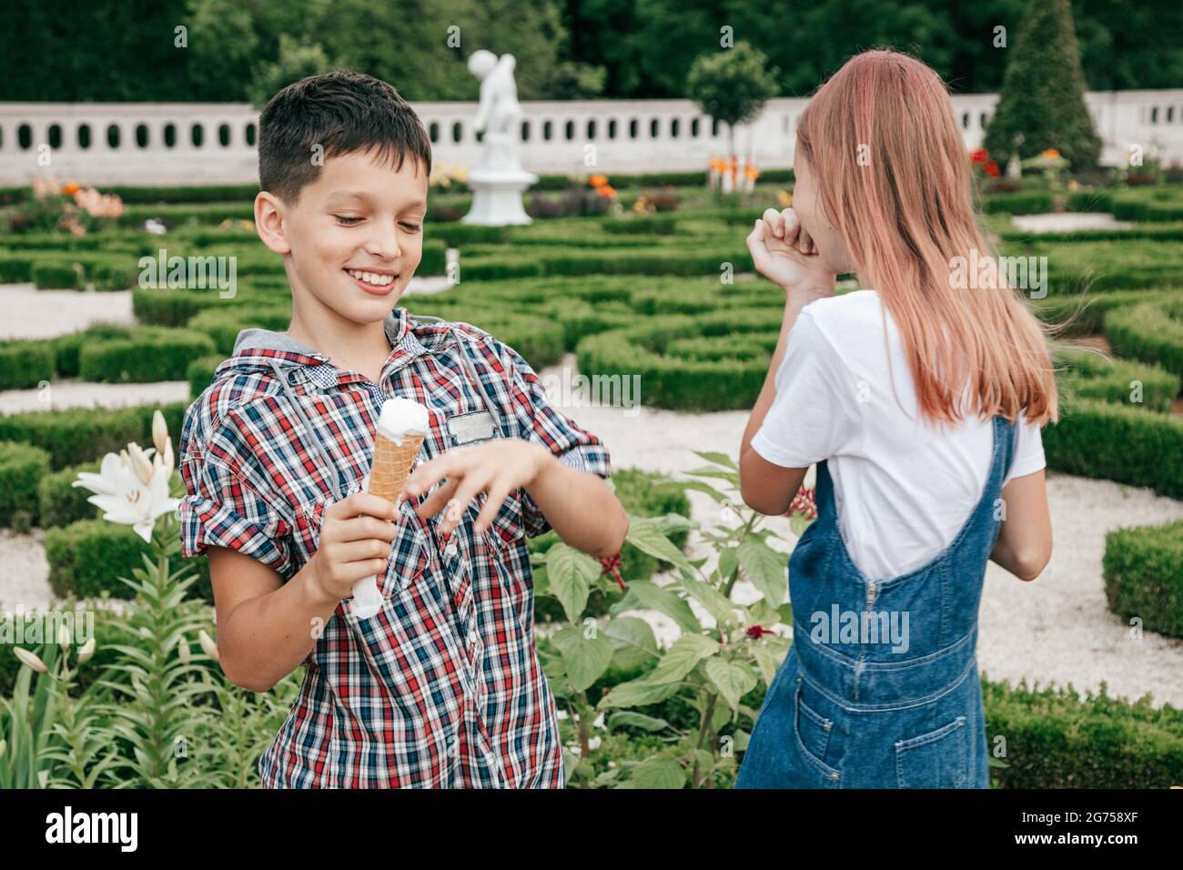 children teenagers boy and girl are having fun on summer day against background of greenery, eating ice cream together Stock Photo