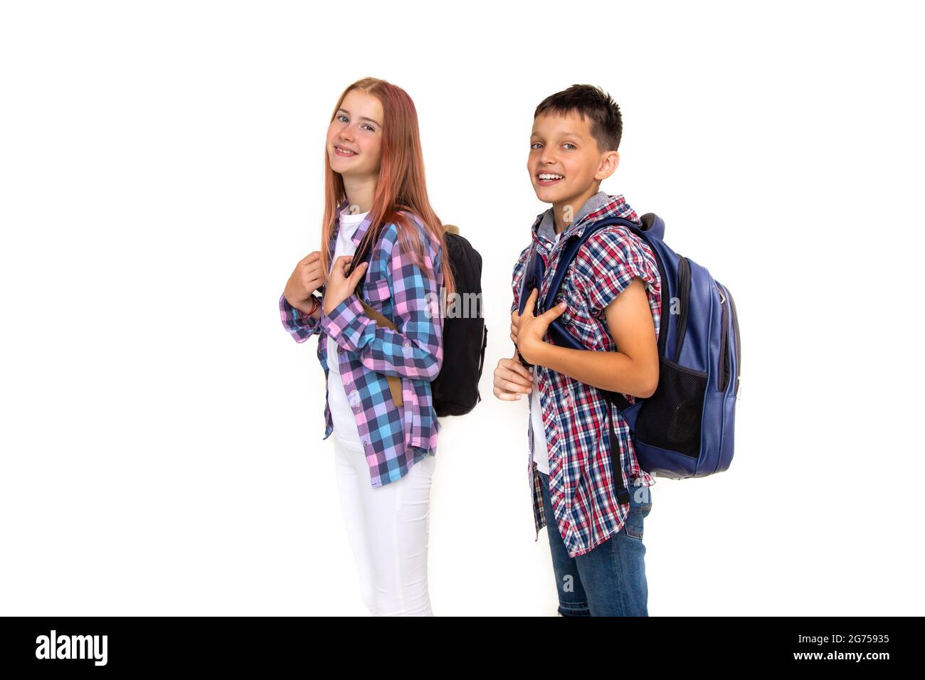 Boy and girl teenager 11 years old schoolboy and schoolgirl looking at camera on white background with backpacks and smiling. Dressed in plaid shirt, Stock Photo