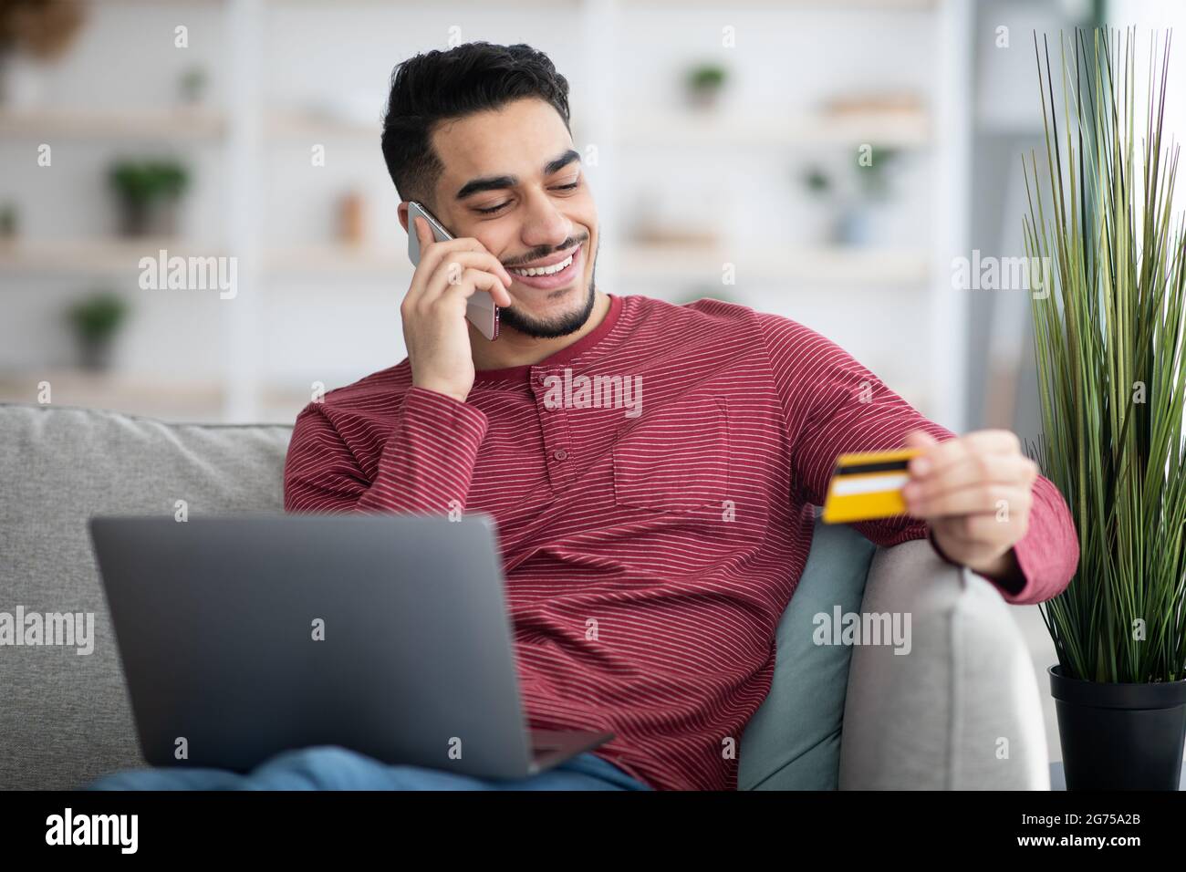 Joyful arab guy holding credit card and having phone conversation Stock ...